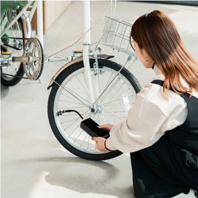 自転車の横にしゃがんで、PANPでタイヤに空気を入れている人